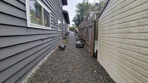 A narrow gravel pathway between two houses with wooden siding.