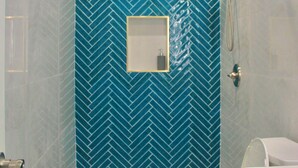 Ein Badezimmer mit blauen Fischgrätfliesen, einer weißen Toilette und einem Duschbereich mit goldener Duschstange.