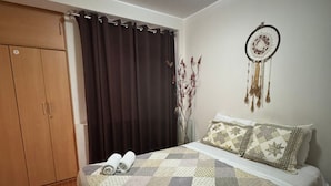 Une chambre à coucher avec un lit, une armoire, un rideau, un attrape-rêves et un vase contenant des fleurs séchées.