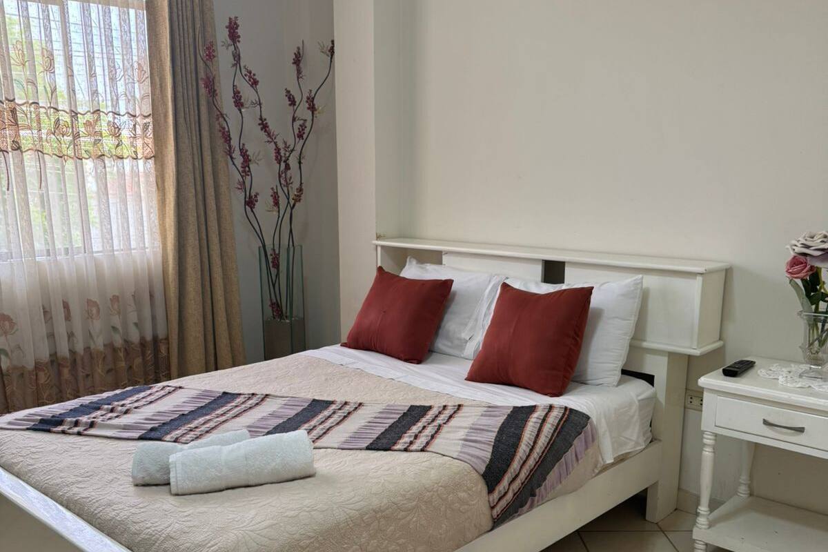 Un dormitorio ordenado con cama, una mesita de noche y un velador.