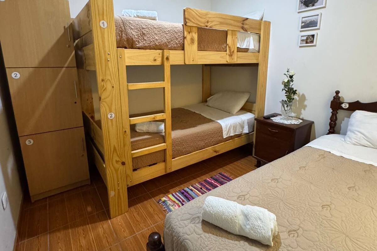 Una habitación pequeña con literas, un armario de madera, una mesita de noche con lámpara y una cama con edredón estampado de flores.