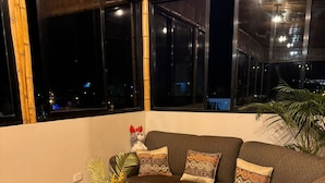 Un salon chaleureux avec un canapé d’angle, une petite table basse agrémentée d’objets décoratifs et de grandes fenêtres offrant une vue sur la ville la nuit.