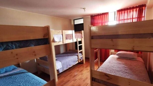 Un dormitorio con tres literas, suelo de madera y una ventana con cortinas rojas.