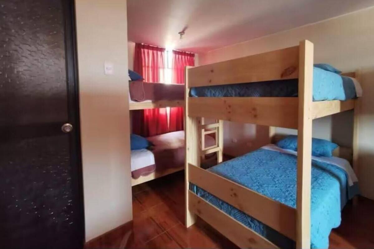 Una habitación con literas, suelo de madera y una puerta que da a otra habitación.