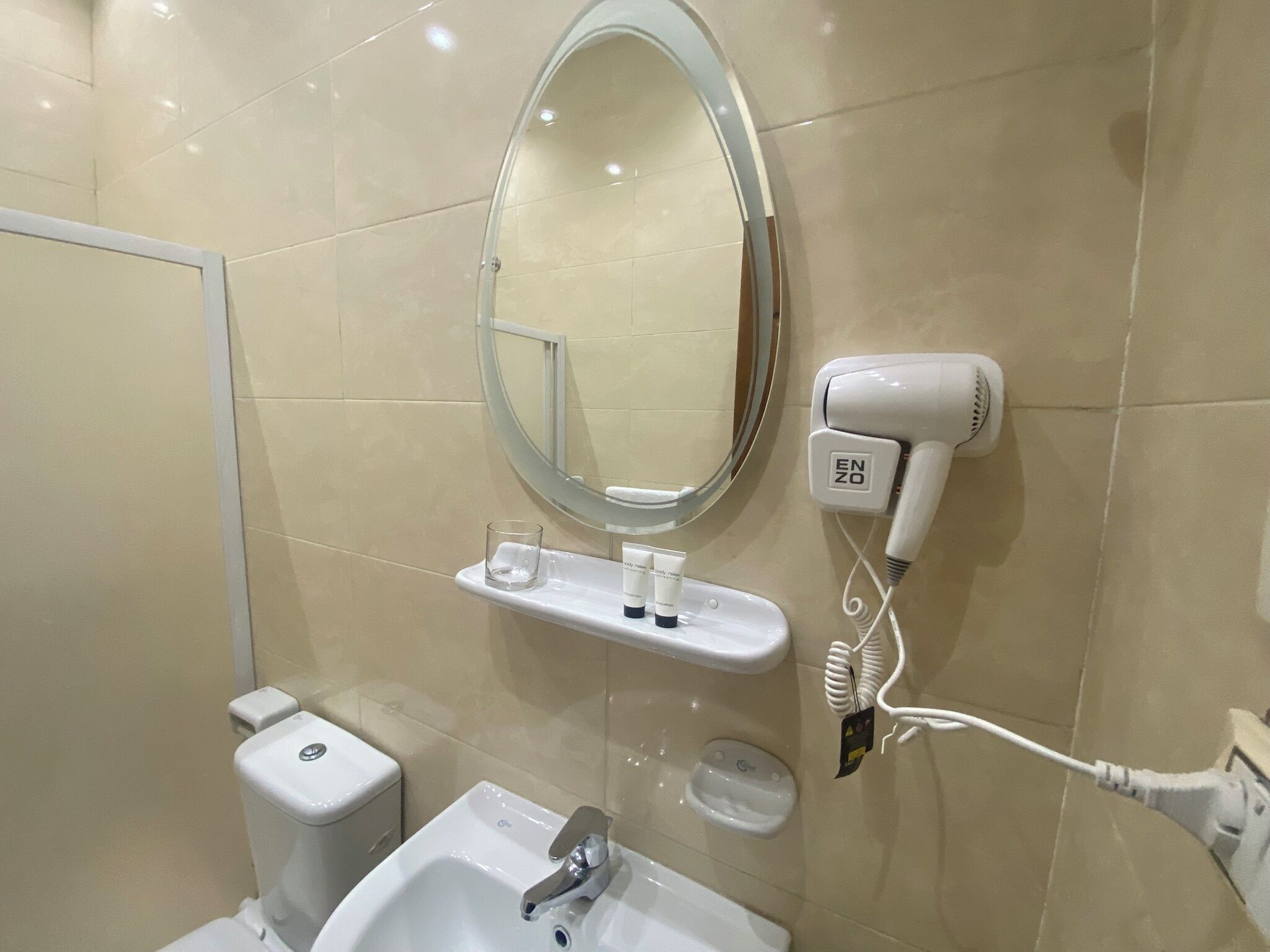 A bathroom with a white sink, a mirror, a hairdryer, and a small shelf with toiletries.