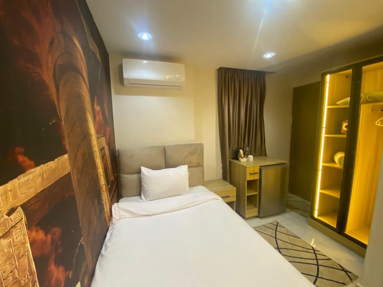 A hotel room with a bed, a desk, a wardrobe, and an air conditioning unit.