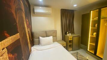 A hotel room with a bed, a desk, a wardrobe, and an air conditioning unit.