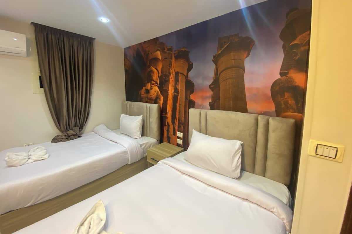 Una camera d'albergo con due letti, un affresco raffigurante rovine antiche e una finestra con tende.