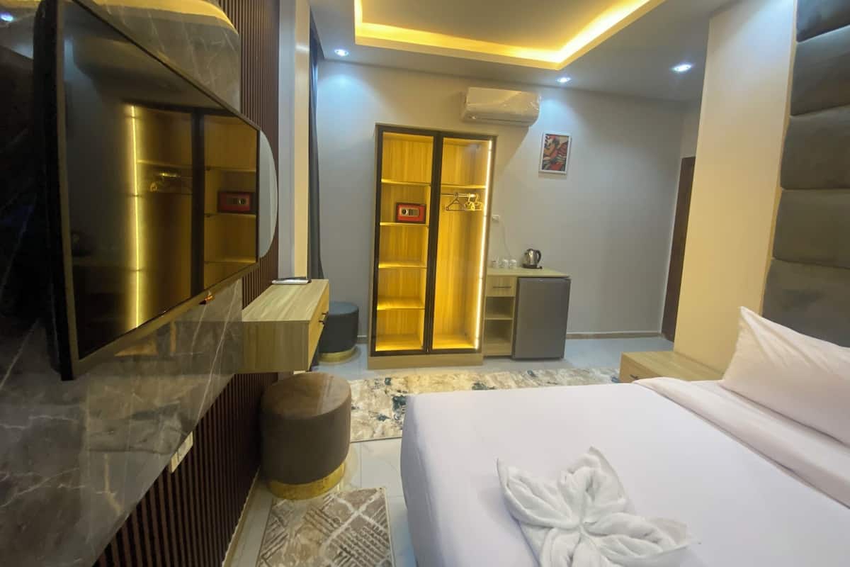 Una camera d'albergo moderna con un letto grande, un comò con specchio, un armadio, un tavolino con bollitore e un condizionatore d'aria a parete.