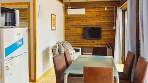 A dining area with a wooden ceiling, a TV mounted on the wall, and a refrigerator with a blue label. - Amazing 2-bedroom bungalow with WiFi, AC in wonderful Punta del Diablo,Uruguay
 (Punta del Diablo)
