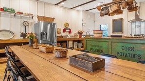A rustic kitchen with wooden furniture, a stainless steel refrigerator, and baskets hanging from the ceiling.