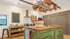 A kitchen with a wooden island labeled 'FARM FRESH PRODUCE', a hanging basket, and a window with a view.