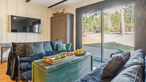 A modern living room with a large TV, a sofa, a coffee table with fruits, and a view of the outdoors.