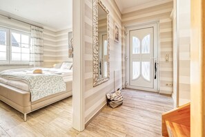 Une chambre à coucher avec un lit, un grand miroir, une porte avec une fenêtre et un petit sac posé sur le sol.