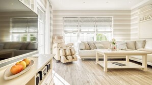 A modern living room with a sofa, a massage chair, a dining table with apples, and large windows. - Rosenberg 27 - "Family-friendly vacation apartment in Zingst with garden and (Zingst)