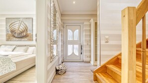 A modern interior with a wooden staircase, a bed with patterned bedding, a hallway with a door, and a wall-mounted mirror. - Rosenberg 27 - "Family-friendly vacation apartment in Zingst with garden and (Zingst)
