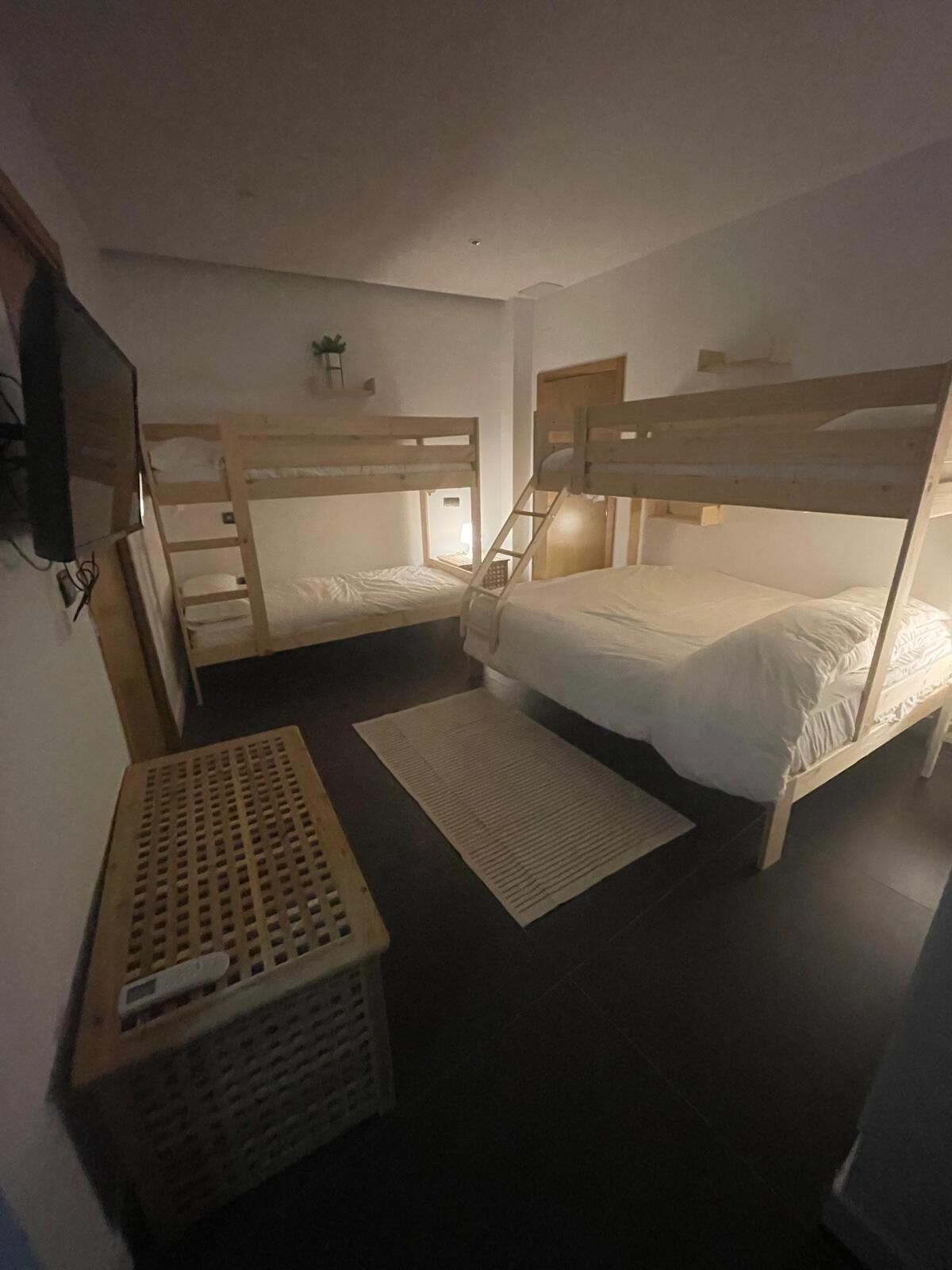 Une chambre de dortoir avec des lits superposés, une petite télévision, une caisse en bois et un tapis sur le sol.