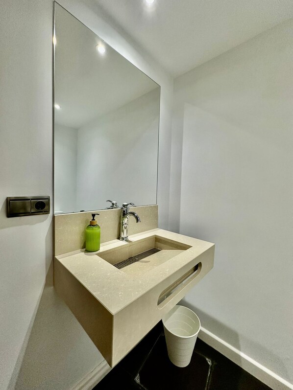 A modern bathroom with a beige sink, a large mirror, and a green soap dispenser.