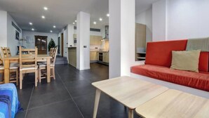 A modern living room with a red sofa, a wooden dining table, and a kitchen in the background.