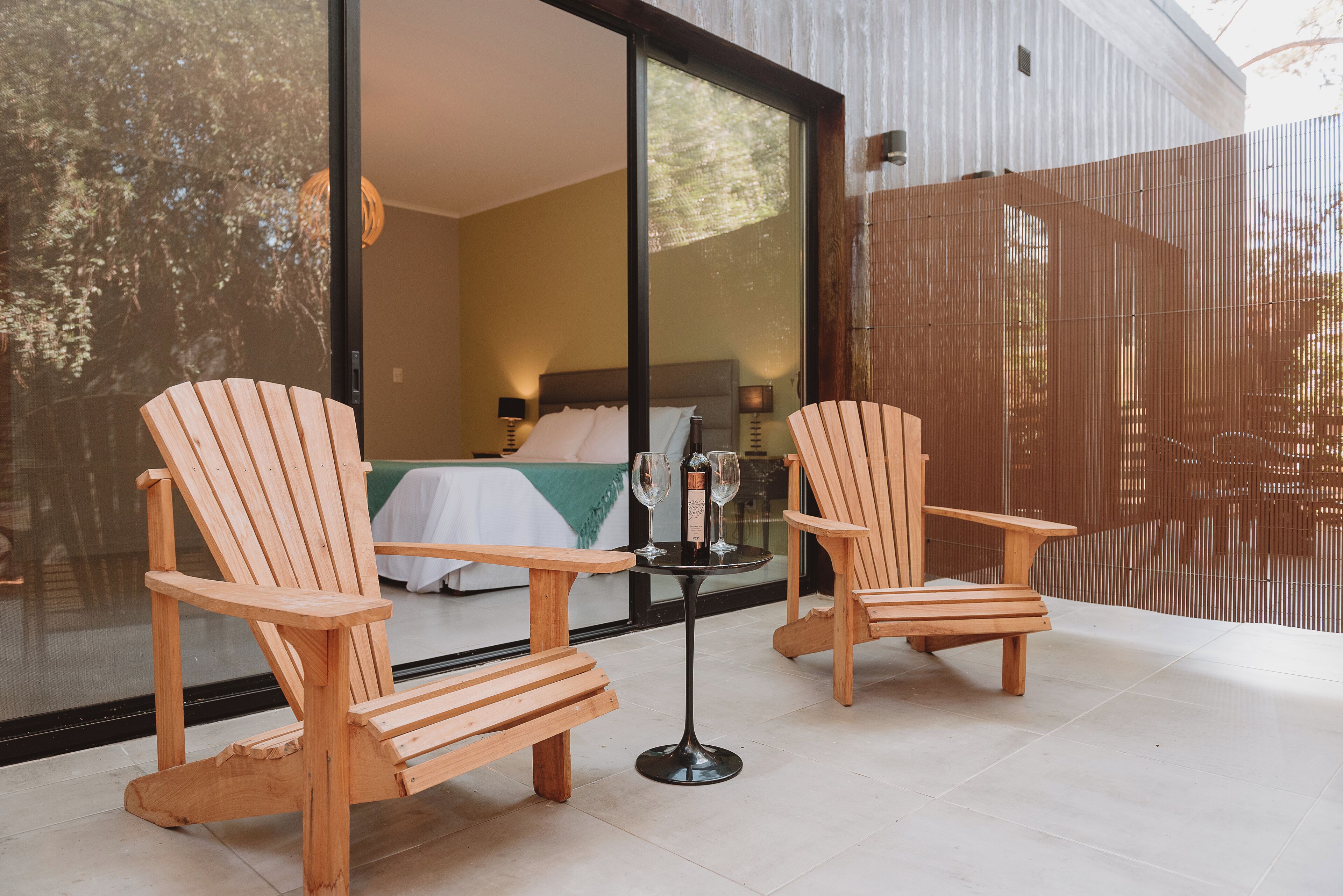 Deux chaises en bois et une petite table avec des verres à vin, le tout sur une terrasse carrelée.