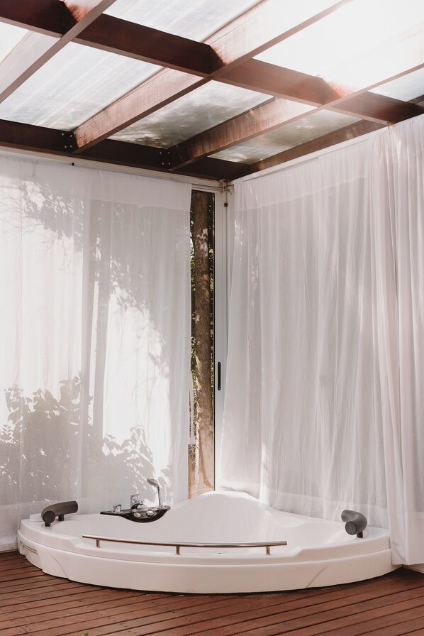 A spa area with a hot tub, wooden flooring, and a pergola with white curtains. - Puerto Dijama Hotel Boutique (Carmelo)