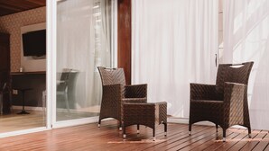 Un espacio exterior soleado con una terraza de madera, una bañera blanca y sillones de mimbre.