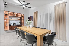 Ein moderner Essbereich mit Holztisch und schwarzen Stühlen, eine Küche mit Holzschränken und einem Deckenventilator.