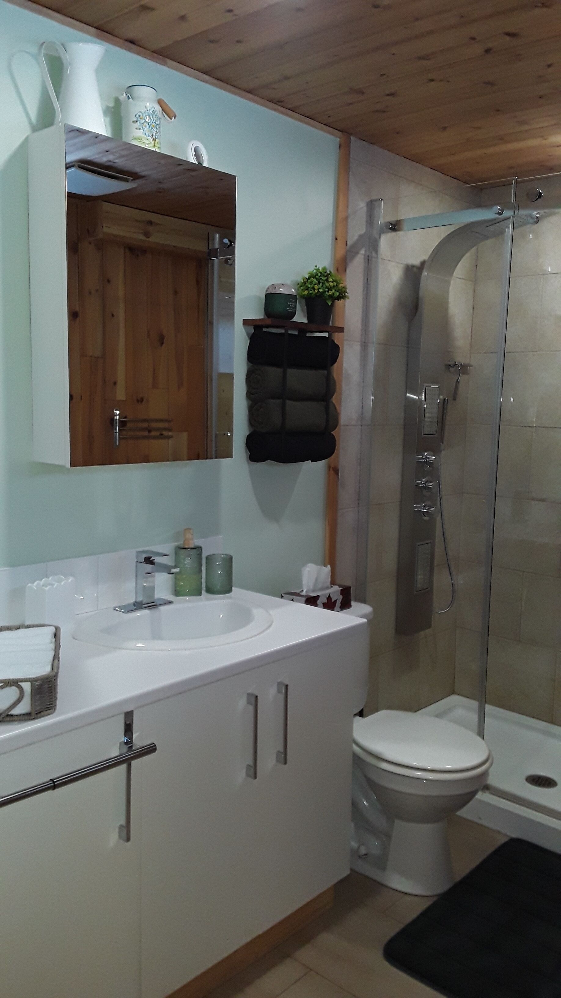 A bathroom with a wooden ceiling, a white sink, a toilet, and a glass shower enclosure.
