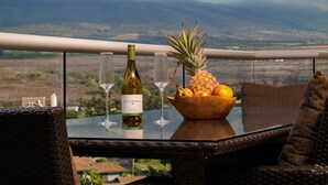 A balcony with a table set for two, featuring a bottle of wine, two glasses, and a bowl of fruit.