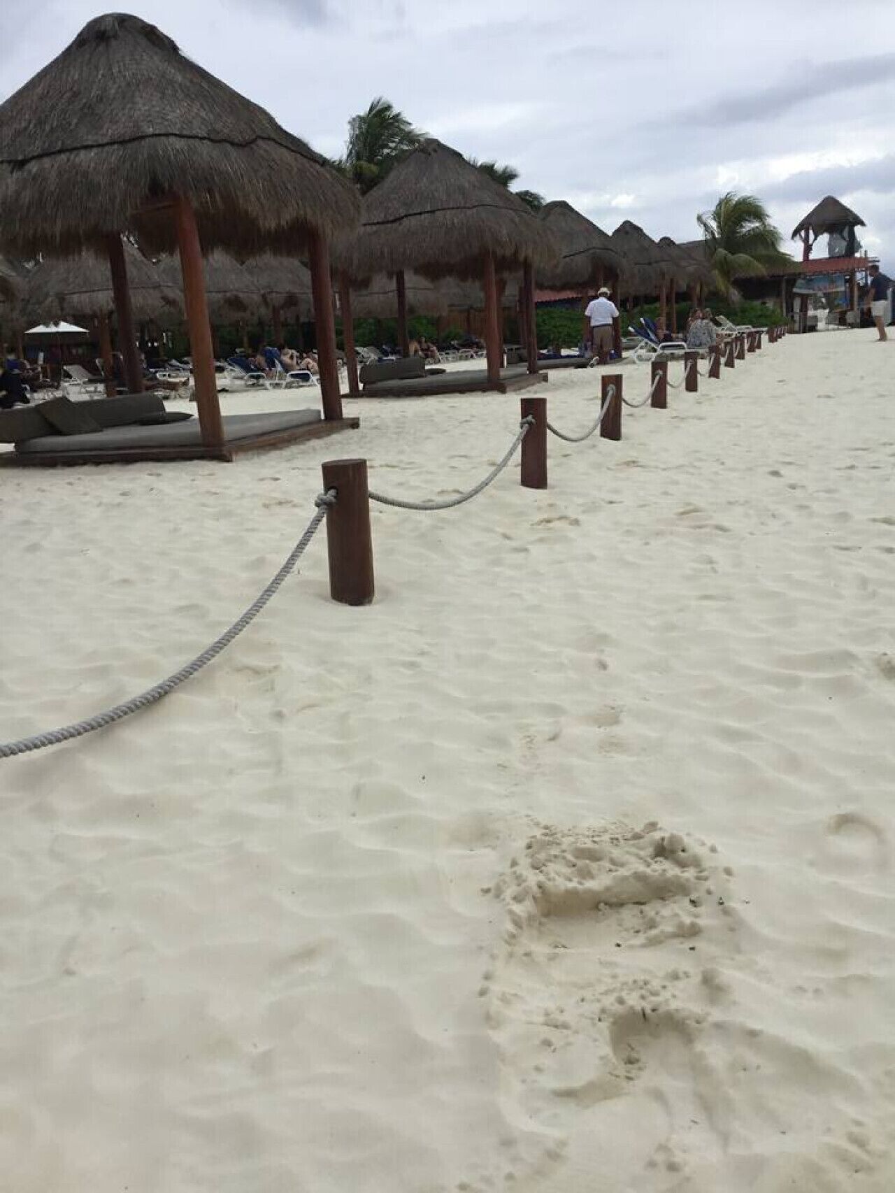 Una playa con sombrillas de paja y sillones de descanso, un paseo marítimo arenoso y un cielo despejado.