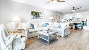 A modern living room with a sectional sofa, a coffee table, and a dining area with a table and chairs. - Wake up to Waves: Stunning Direct Ocean Front View with Heated Pool & Hot Tub! (Cocoa Beach)