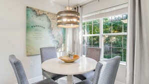 Un comedor con una mesa redonda, sillas tapizadas en gris, una lámpara colgante y un mapa de Florida en la pared.