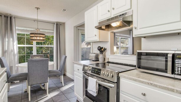 Una cocina moderna con muebles blancos, horno empotrado, microondas y un comedor con mesa y sillas.