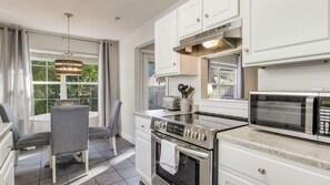 Una cocina moderna con muebles blancos, horno empotrado, microondas y un comedor con mesa y sillas.