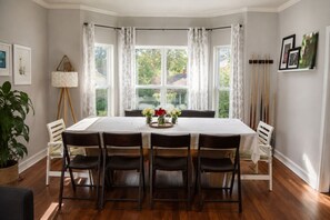 A dining room with a rectangular table, six chairs, a vase with flowers, and a window with curtains.