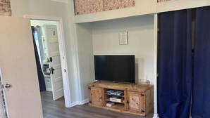 A living room with a TV on a wooden stand, a patterned rug, and a door leading to another room. - Unit 17 King suite kitchen Fast Wifi Smart TV (Hot Springs)