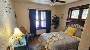 A bedroom with a bed, a desk with a lamp, a window with curtains, a ceiling fan, and a plant. - Charming 2-bedroom, cozy bungalow with sunroom in fabulous St. Louis with WiFi (St. Louis)