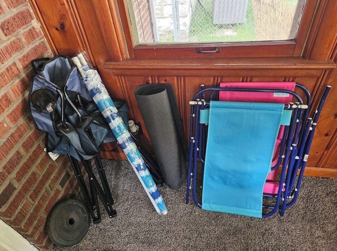 A wheelchair, a rolled-up mat, and a blue and pink mobility aid against a wooden door and window.