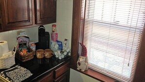 A kitchen with wooden cabinets, a countertop with various items, a window with blinds, and a chair with a floral seat. - Charming 2-bedroom, cozy bungalow with sunroom in fabulous St. Louis with WiFi (St. Louis)
