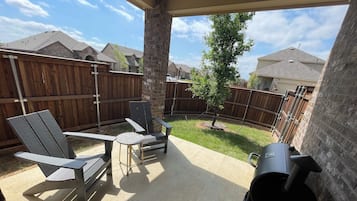 Une terrasse extérieure équipée d’un barbecue, de deux fauteuils Adirondack et d’une petite table.