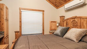 Een slaapkamer met een houten hoofdbord, een groot bed, een raam met jaloezieën en een airconditioning.