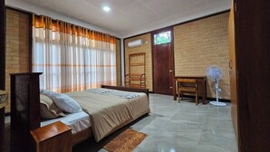 A bedroom with a bed, a desk, a chair, a standing fan, and a window with curtains. - Seagulls Garden -450 m to beach & Free* Utility (Hikkaduwa)