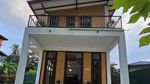 A two-story building with a balcony, a covered entrance, and a grassy area in front. - Seagulls Garden -450 m to beach & Free* Utility (Hikkaduwa)
