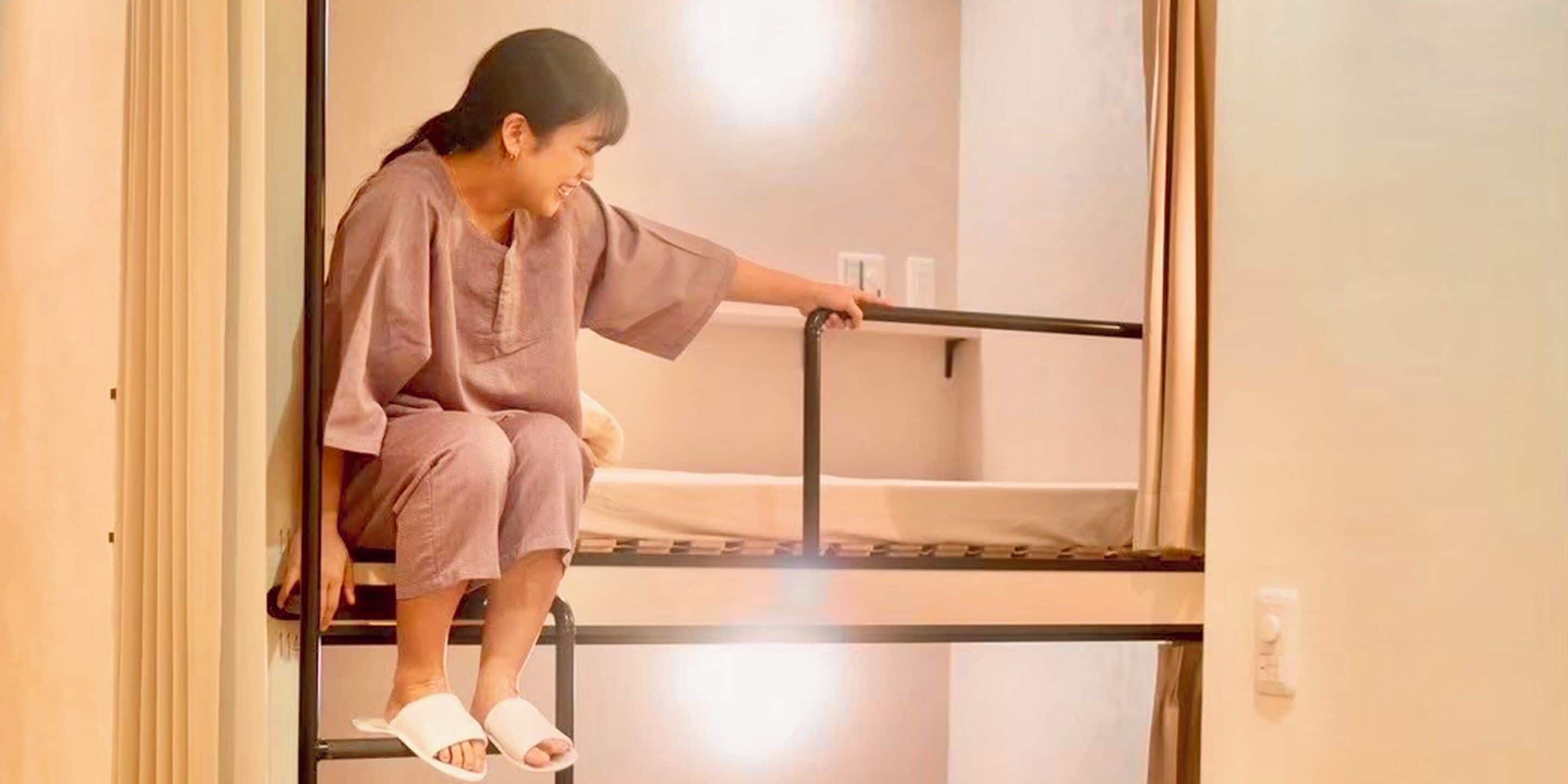 A person sitting on a bunk bed in a room with a simple, functional design.