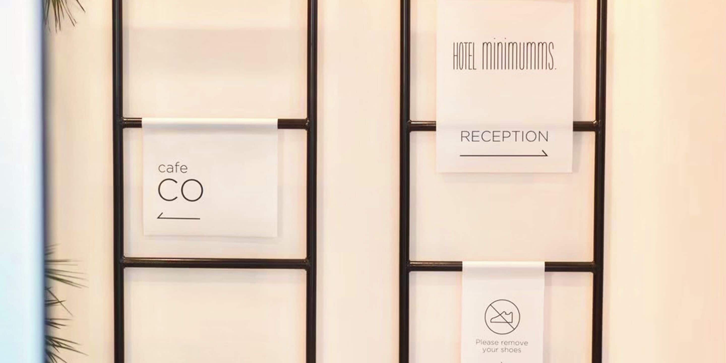 Un mur orné de panneaux encadrés indiquant les services offerts par l’hôtel, tels qu’un café, une réception et les règles concernant le retrait des chaussures.