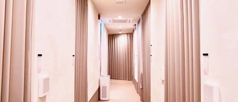 A hotel hallway with a central air conditioning unit, a hand sanitizer dispenser on the wall, and a ceiling-mounted light fixture.