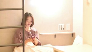 Eine Person sitzt auf einem Bett in einem Raum mit einer Etagenbett-Konstruktion und benutzt ein Smartphone.