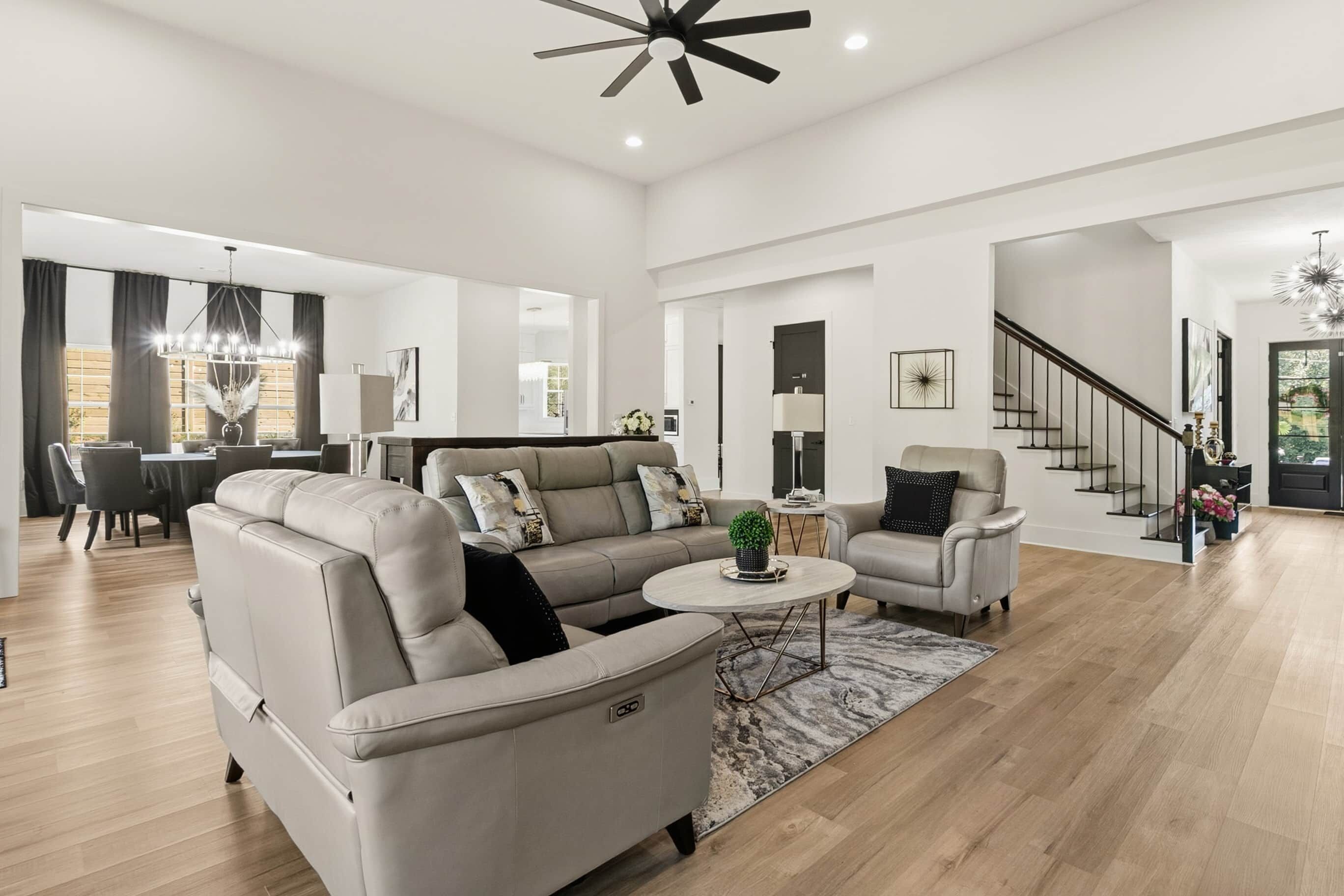 A spacious living room with a sofa, armchairs, a coffee table, and a staircase leading to an upper level.