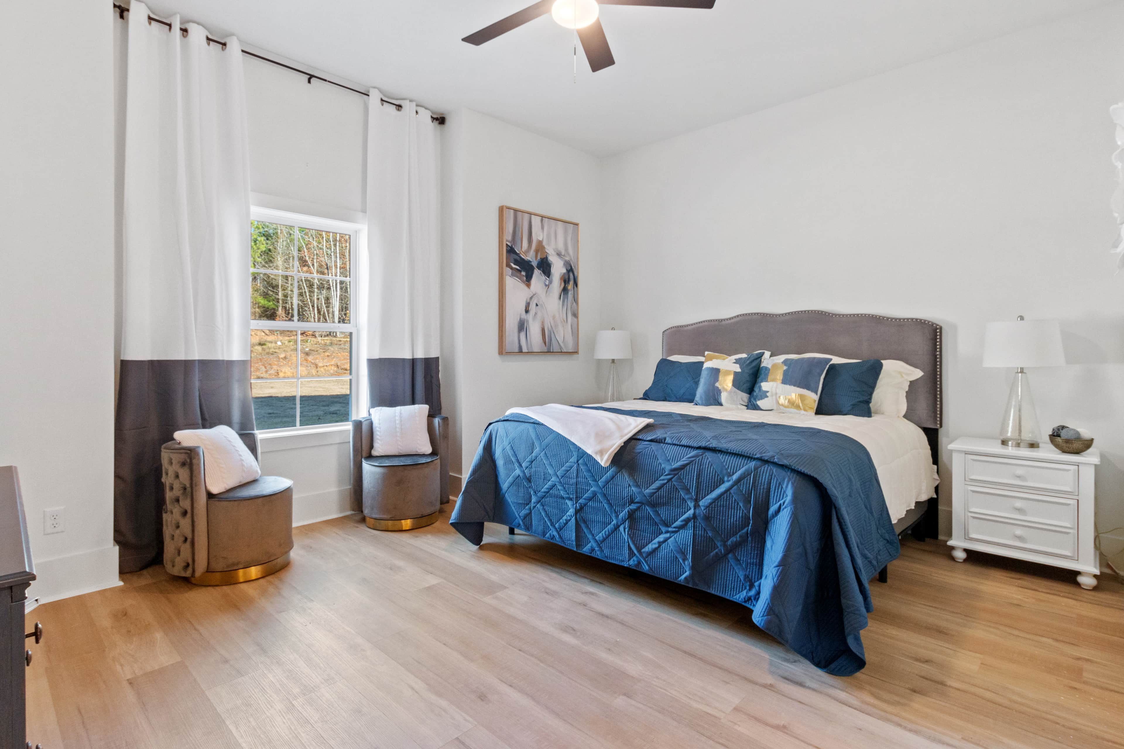 A bedroom with a bed, bedside tables, a window with curtains, and a ceiling fan.