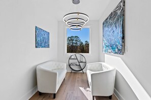 En modern inredning med två vita fåtöljer, en rund hylla i metall och abstrakta målningar.